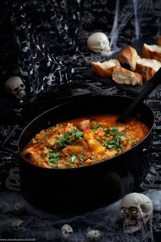 a black pot filled with soup next to bread and skulls on the table in front of it