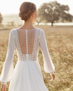 the back of a woman's wedding dress in a field with trees and grass