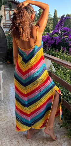 a woman in a colorful crocheted dress is standing on a patio with her hands behind her head