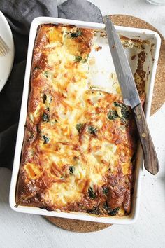 a casserole dish with cheese and spinach in it next to a knife