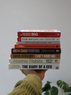 a person holding a stack of books over their head in front of a potted plant