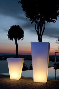 two large planters sitting next to each other on a wooden deck at dusk with a tree in the background