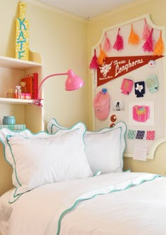 a bed with white pillows and pink lamps on the headboard next to a shelf