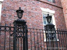 an iron gate is in front of a brick building with a clock on the side