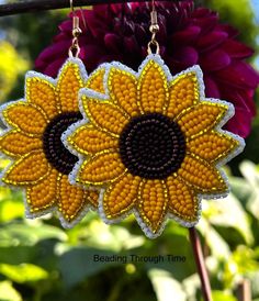 a pair of sunflower earrings hanging from a hook on a branch with flowers in the background