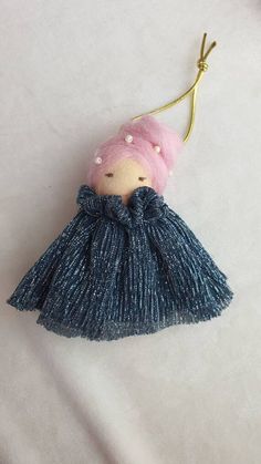 a small doll with pink hair wearing a blue dress and holding a gold keychain