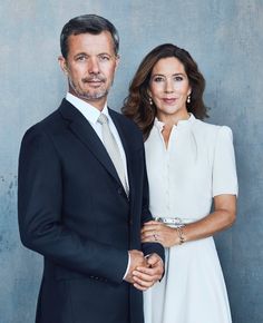 a man and woman standing next to each other in front of a gray wall wearing suits