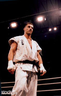 a man standing on top of a wrestling ring wearing a white suit and holding a black belt