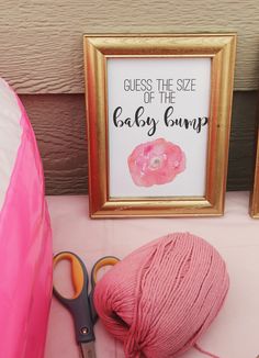 a pink ball of yarn next to a pair of scissors and a sign that says guess the size of the baby bump