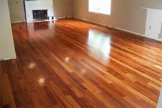 an empty room with hard wood flooring and fireplace in the corner, looking into the living room