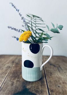 a white and black polka dot mug with flowers in it on a wooden table next to a plant