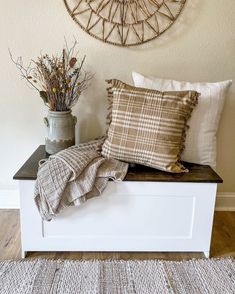 a white bench topped with pillows next to a vase filled with dried flowers and plants