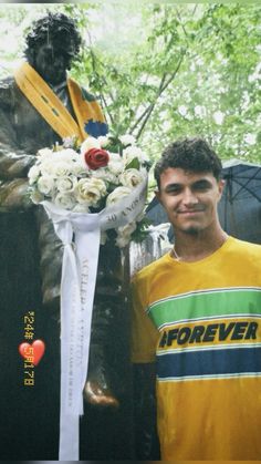 a man standing in front of a statue with flowers on his lap next to him