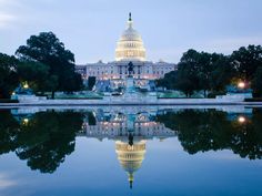 the united states capitol building is lit up at night with its reflection in the water