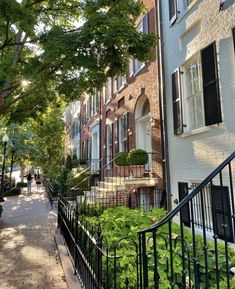 a row of brick townhouses with black iron railings and green plants on the sidewalk