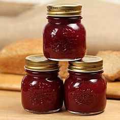 three jars filled with jam sitting on top of a wooden table next to sliced bread