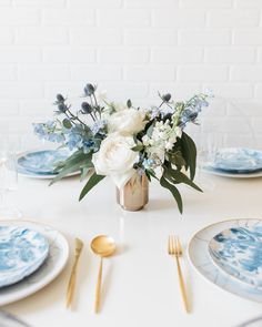 a table set with blue and white plates, silverware and flowers in a vase