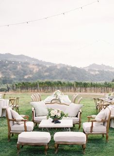 an outdoor seating area with chairs and tables in the grass, surrounded by greenery