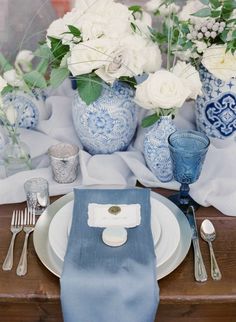 the table is set with blue and white dishes, silverware, and vases