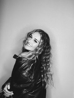 a black and white photo of a woman wearing a leather jacket with her hair blowing in the wind