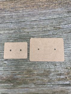 two square tags sitting on top of a wooden table with holes in the paper to place them