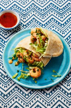 a wrap with shrimp and lettuce on a blue plate next to dipping sauce