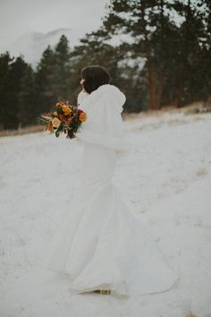 a woman in a white wedding dress walking through the snow with flowers on her bouquet