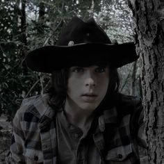 a woman wearing a black cowboy hat next to a tree