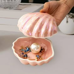 a pink shell shaped container with pearls and other jewelry in it on a white table