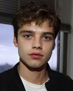 a close up of a person wearing a black jacket and white t - shirt with a window in the background