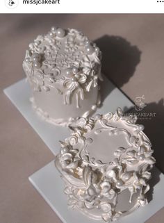 two white cakes sitting on top of a plate covered in frosting and pearls,