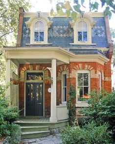 a brick house with white trim and black door, surrounded by greenery on both sides