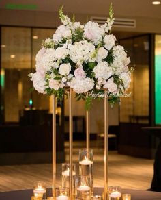 a tall vase filled with lots of white flowers on top of a table next to candles