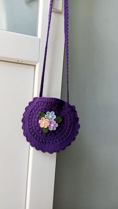 a purple crocheted purse hanging on the side of a white door with flowers