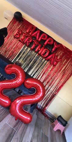 a man standing in front of a red happy birthday sign with balloons and streamers