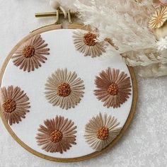 a close up of a embroidery on a white surface with flowers in the center and feathers around it