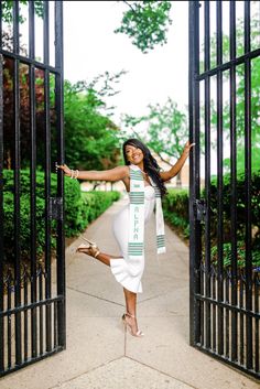 a woman is posing in front of an iron gate with her arms outstretched and legs spread out