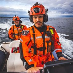 two men in orange life jackets are on a boat and one is looking at the camera