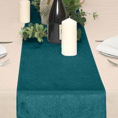 the table is set with white candles and green linens, along with greenery