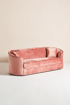 a pink velvet couch sitting on top of a white table next to a beige wall