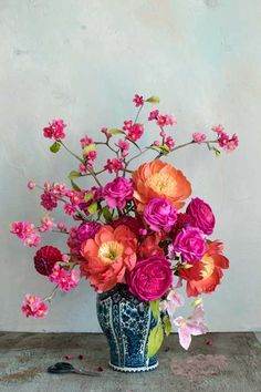 a blue and white vase filled with lots of pink and red flowers on top of a wooden table