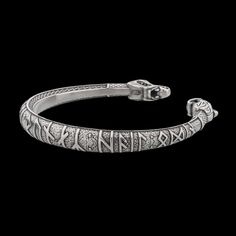 a silver bracelet with intricate designs on the sides and an open clasp at the end