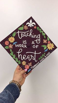 a person holding up a graduation cap that says teaching works as heart with florets on it