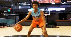 a young man holding a basketball on top of a hard wood floor in an indoor court