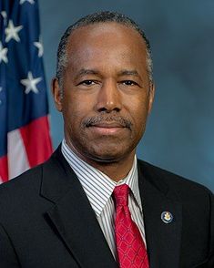 a man wearing a suit and tie in front of an american flag