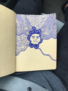 an open notebook with a blue and white drawing on it's cover, sitting in someone's lap