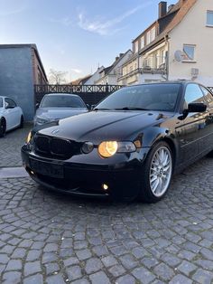 a black car parked in front of a building on a cobblestone street next to other cars