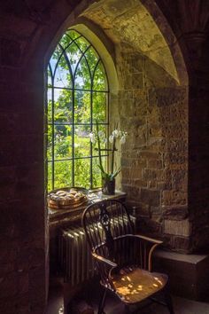 an arched window in a stone building with a wooden chair and potted plant next to it