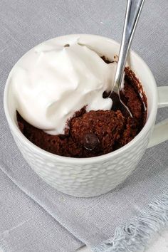 a cup filled with ice cream sitting on top of a white table cloth next to a spoon