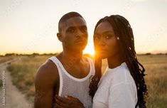 a man and woman standing together in the middle of an open field at sunset or sunrise